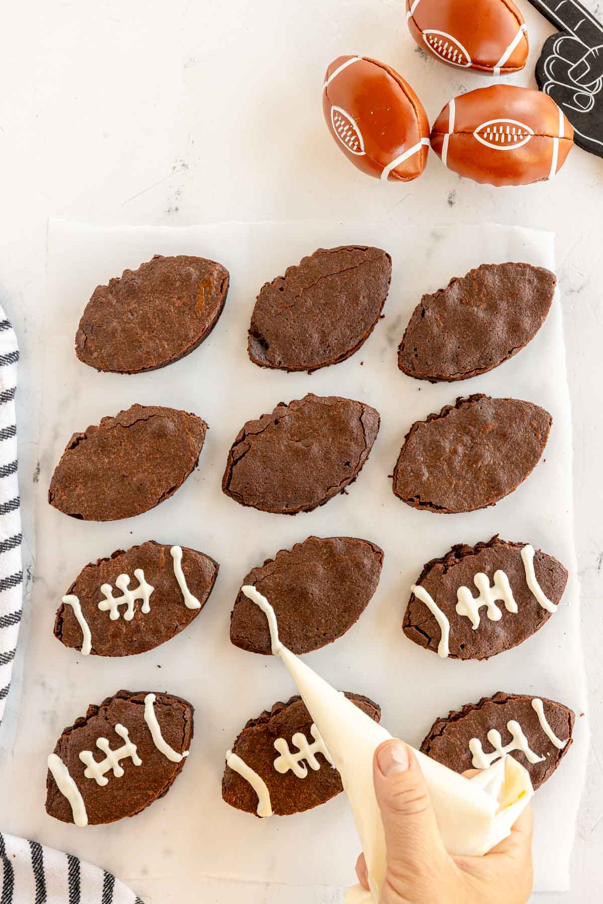 hand decorating football brownies with white icing