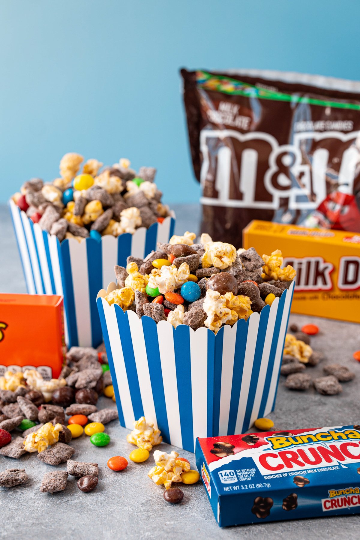 popcorn snack mix in a blue popcorn bucket with a bunch of candy around